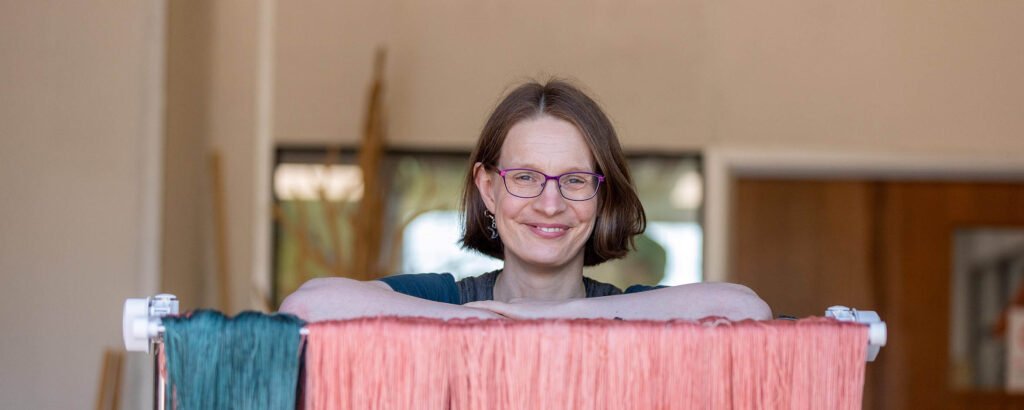 Rachel Moutrie, founder of Yarn Adventure and hand dyer at Skein Queen, leaning on a rack of yarn hung up to dry