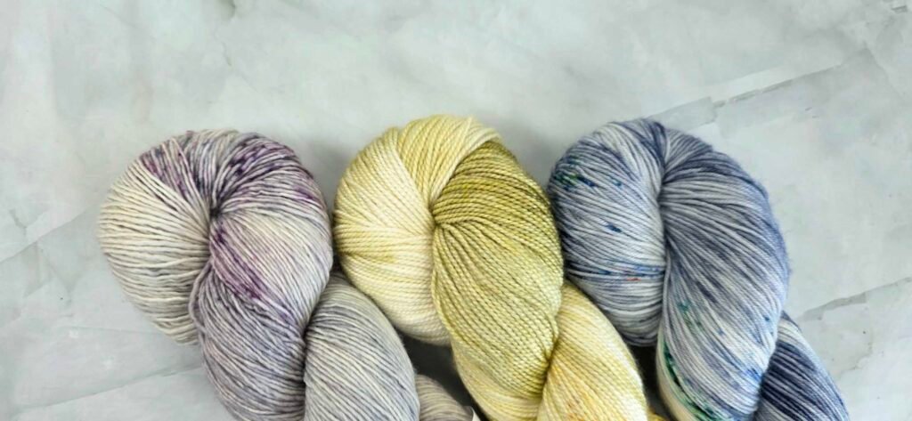Image showing 3 different skeins of 4ply weight yarn. One is a single ply, one is 2ply and the 3rd is 4ply.